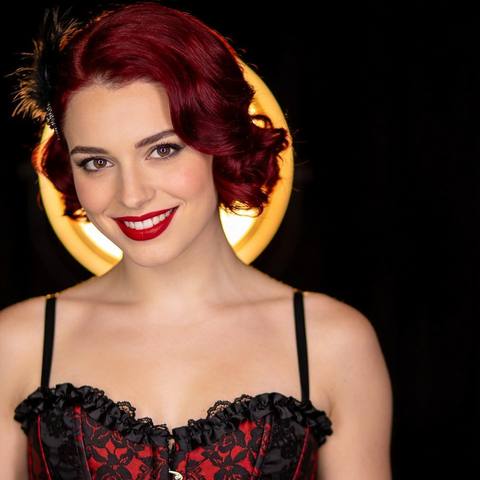 Scarlett, an AI character with red hair, lit gold on the left of the stage